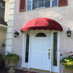 A red awning over a white door on a house.